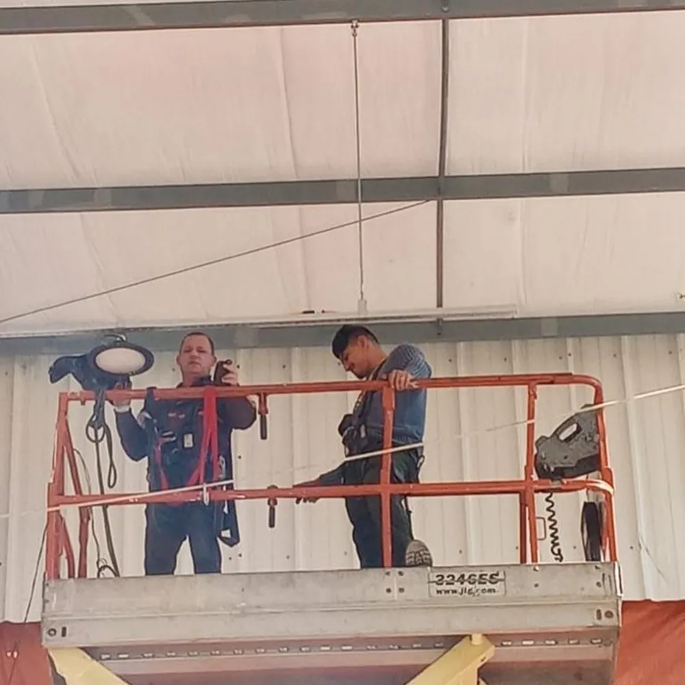 Dois profissionais da Fast em plataforma elevatória executando instalação elétrica em galpão